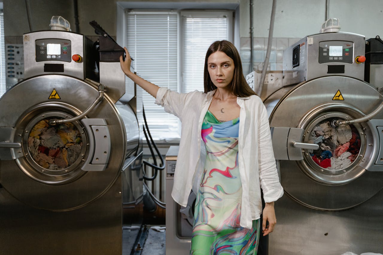 Confident woman in colorful dress at a laundromat with industrial washing machines.